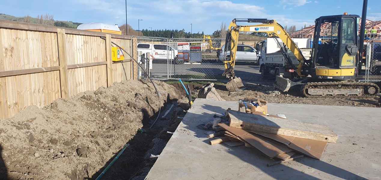 Smart Contracting excavator digging a drainage trench beside a Christchurch new build
